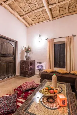 a living room with two beds and a table with a bowl of fruit at Riad Madu in Merzouga