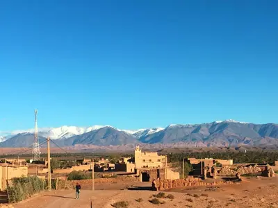 a person walking down a dirt road in a village with mountains at Auberge Migusta in Skoura