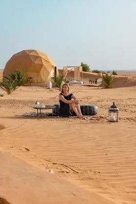a woman sitting on the sand in the desert at Sunrise Sahara Camp in Merzouga