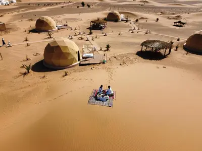 two people sitting on a table in the desert at Sunrise Sahara Camp in Merzouga