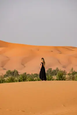 a woman standing on a sand dune in the desert at Sunrise Sahara Camp in Merzouga