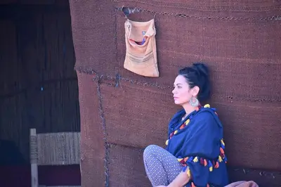 a woman sitting in a chair next to a wall at Tikida Camp by tinfou in Zagora