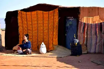 a woman sitting on the ground in front of a building at Tikida Camp by tinfou in Zagora
