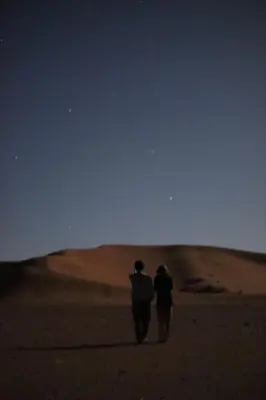 two people walking in the desert at night at Tikida Camp by tinfou in Zagora
