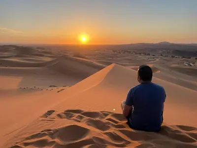 a man sitting in the desert watching the sunset at Chigaga Desert Camp in Mhamid