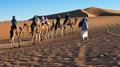 a group of people riding camels in the desert at Chigaga Desert Camp in Mhamid