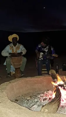 a group of people sitting around a fire at Chigaga Desert Camp in Mhamid