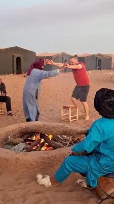 a group of people standing around a fire on the beach at Chigaga Desert Camp in Mhamid