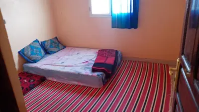 a small bed in a room with a striped carpet at Chez zakaria guest house in Merzouga