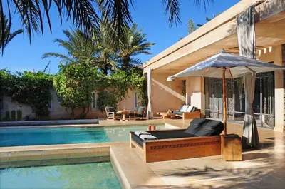 a pool with a bed and an umbrella next to a house at Palais Namaskar in Marrakech