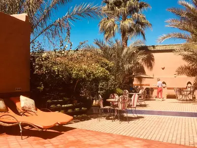 a patio with chairs and tables and palm trees at Le Sauvage Noble in Tissergat