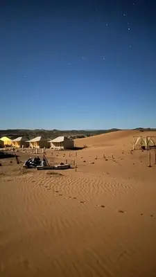 a beach with umbrellas and people in the sand at Original Desert Camp in Merzouga