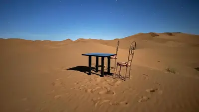 a table and a chair sitting in the desert at Original Desert Camp in Merzouga