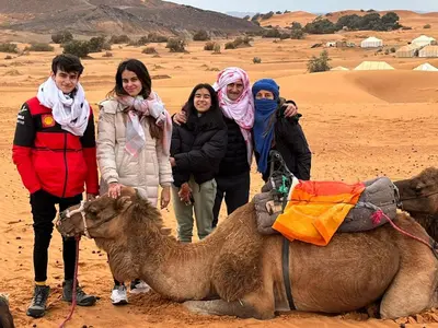 a group of people standing next to a camel in the desert at Original Desert Camp in Merzouga