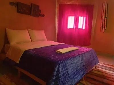 a bedroom with a bed with a purple blanket and a window at ecolodge bivouac des aigles in Ouarzazate