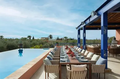 a long dining table with chairs next to a swimming pool at Le Clos des Oliviers in Oulad Jellal