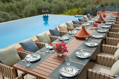 a long table with plates and glasses next to a pool at Le Clos des Oliviers in Oulad Jellal