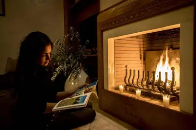 a woman reading a book in front of a fireplace at Dar Neylla in Douar Caïd Layadi