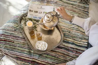 a person sitting on a bed with a tray with a tea set at Dar Neylla in Douar Caïd Layadi