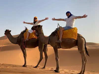 two men riding on the backs of camels in the desert at Bivouac Erg Chegaga Nomademoi in El Gouera