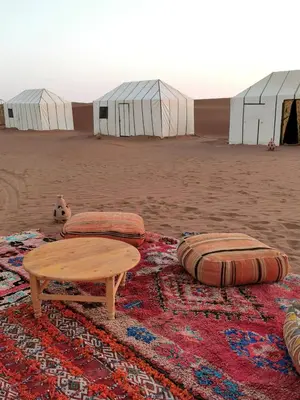 a table and pillows on a rug in front of tents at Bivouac Erg Chegaga Nomademoi in El Gouera