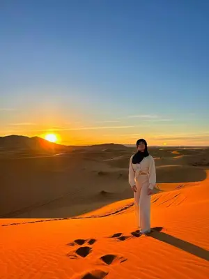 a woman standing in the desert at sunset at Desert Backpackers Camp in Merzouga