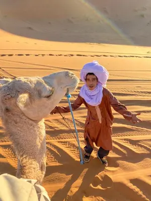 a woman walking in the desert with a camel at Desert Backpackers Camp in Merzouga