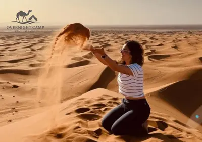 a woman sitting on the sand in the desert at Overnight Camp Erg Chebbi in Merzouga