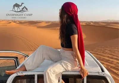 a woman sitting on the roof of a vehicle in the desert at Overnight Camp Erg Chebbi in Merzouga