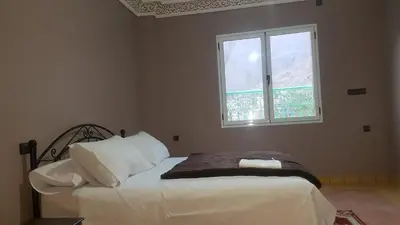 a bedroom with a bed with white sheets and a window at Auberge Restaurant Fatihi Freres in Tinerhir