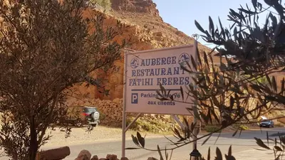 a sign in front of a building with a mountain in the background at Auberge Restaurant Fatihi Freres in Tinerhir