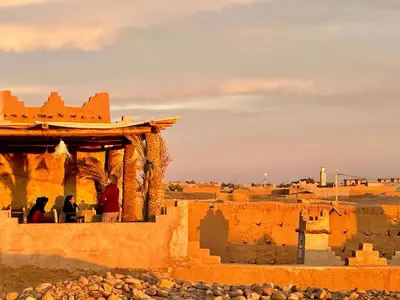 two people sitting on a balcony of a building in the desert at Auberge Kasbah Dar Sahara Tours in Mhamid