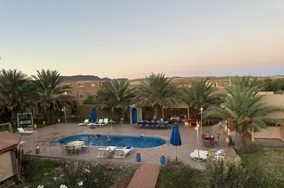 an outdoor pool with palm trees and tables and umbrellas at Oasis Tilogui-Luxury Hotel Restaurant and Desert Excursions In Zagora in Zagora