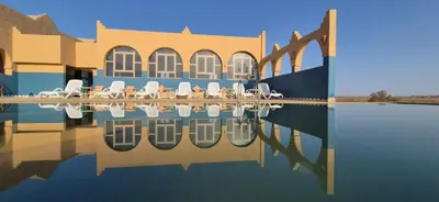 a building with chairs and a reflection in the water at Takojt in Merzouga