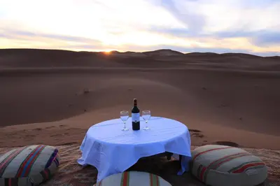 a table with a bottle of wine and two wine glasses at Luxury Berber Camp in El Gouera