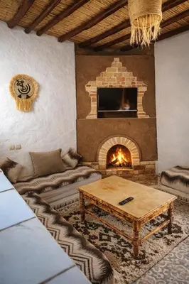 a living room with a fireplace and a table at Chez aubazine in Merzouga