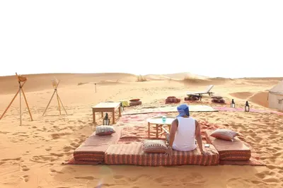 a woman sitting on a bed in the desert at Desert Luxury Camp Morocco in Merzouga