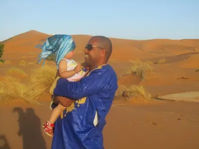 a man holding a child in the desert at Desert Luxury Camp Morocco in Merzouga