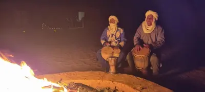a group of three people sitting next to a fire at Chigaga Luxury Camp in Mhamid