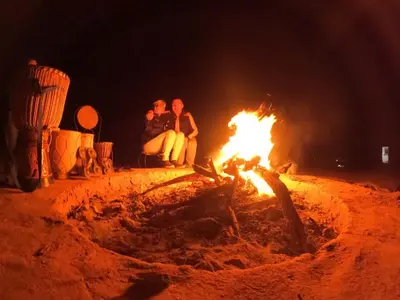 three people sitting around a fire at night at Chigaga Luxury Camp in Mhamid