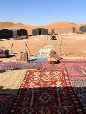 a rug on the ground in a desert with windmills at Chigaga Luxury Camp in Mhamid