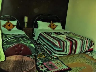 a bedroom with two beds and a chair and a rug at Tifinagh Guest House in Merzouga