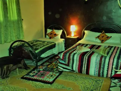 a bedroom with two beds and a table with a lamp at Tifinagh Guest House in Merzouga