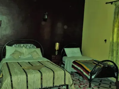 a bedroom with two beds and a chair at Tifinagh Guest House in Merzouga