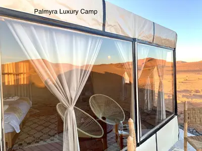 a tent in the desert with a bed and chairs at Palmyra Luxury Camp in Merzouga