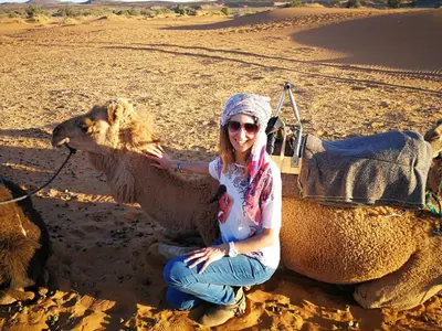 a woman kneeling next to a camel in the desert at Desert Luxury Tented & Activities in Hassilabied