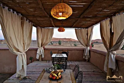 a table and chairs on a porch with a view of the desert at Sunrise Palace Merzouga in Merzouga