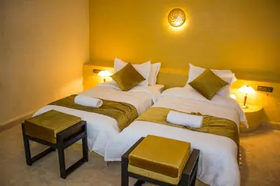 two beds in a room with two tables and two lamps at Dar Morocco in Merzouga