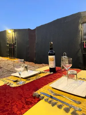 a bottle of wine sitting on a table with glasses at Nomada Desert Camp in Merzouga