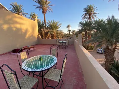 a patio with a table and chairs and palm trees at Camp Auberge Sahara Marokko in Mhamid